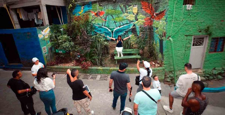 Descripción: Hombres y mujeres mirando mural en comuna de Cali, en medio de la calle.