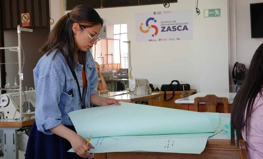 Descripción: Mujer revisando papeles grandes sobre una mesa.